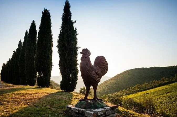 A black rooster statue silhouetted against cypress trees and Chianti hills