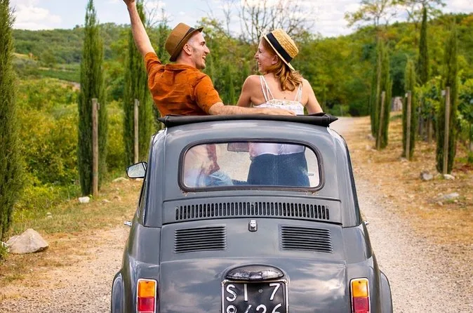 A vintage Fiat 500 with an open roof driving down a cypress-lined lane